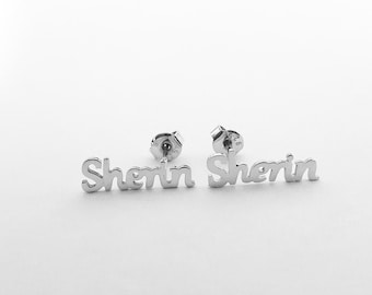 Könnte beinhalten: Ein Paar silberfarbene Ohrstecker mit dem Namen "Sherin" in Schreibschrift. Die Ohrringe sind vor einem weißen Hintergrund platziert, wodurch ihr Design hervorgehoben wird.