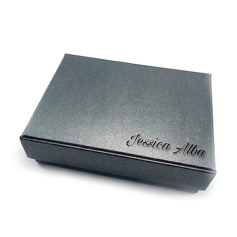 K&ouml;nnte beinhalten: Eine graue Geschenkbox mit dem Namen "Jessica Alba" auf der Oberseite.