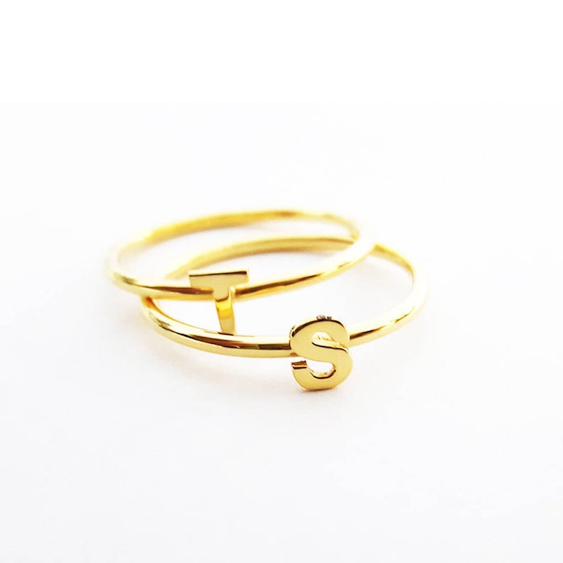 K&ouml;nnte beinhalten: Zwei goldene Ringe mit den Buchstaben "T" und "S" darauf.