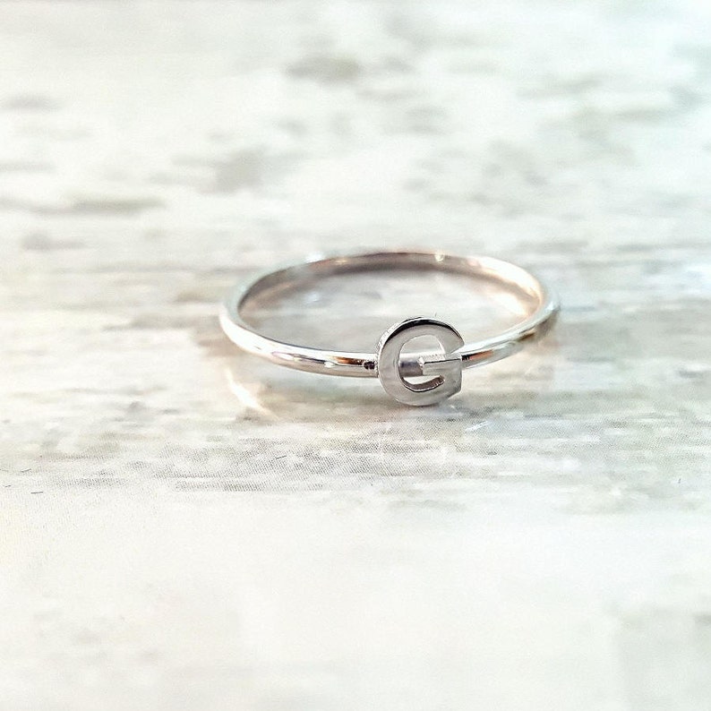 K&ouml;nnte beinhalten: Ein silberner Ring mit einem Buchstaben G.