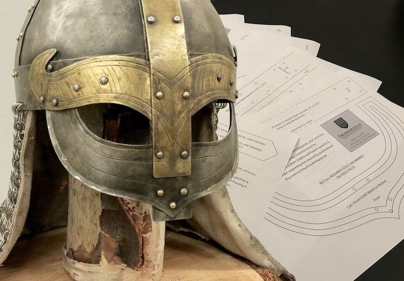 Op de afbeelding: Een close-up van een middeleeuwse helm met een messing rand en kettingmail. De helm staat op een houten standaard en wordt vergezeld door een papieren patroon met instructies voor het maken van een vergelijkbare helm.