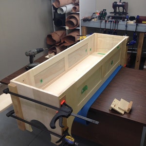 Peut inclure: Une bo&icirc;te en bois avec un rev&ecirc;tement de protection bleu est assembl&eacute;e &agrave; l'aide de pinces. La bo&icirc;te est en bois clair et a un design simple. La bo&icirc;te est en cours de construction sur une table en bois brun.
