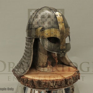 Op de afbeelding: Een zilveren Vikinghelm met een gouden rand en een kettingbaard. De helm staat op een houten standaard.