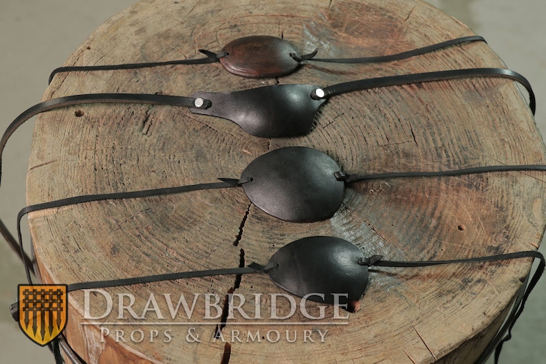 Four different black eye patches with leather thonging siting on a natural wooden tree stump from Drawbridge Props and Armoury.