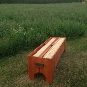Peut inclure: Un coffre en bois avec un couvercle &agrave; charni&egrave;res, ouvert pour r&eacute;v&eacute;ler des planches de bois &agrave; l'int&eacute;rieur. Le coffre est teint&eacute; d'une couleur brun rouge&acirc;tre et poss&egrave;de une poign&eacute;e en m&eacute;tal sur le devant.