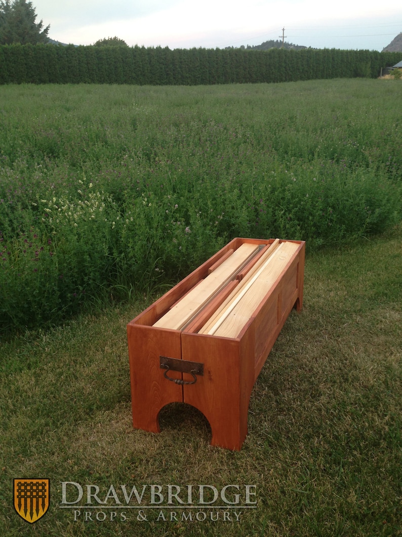 Peut inclure: Un coffre en bois avec un couvercle &agrave; charni&egrave;res, ouvert pour r&eacute;v&eacute;ler des planches de bois &agrave; l'int&eacute;rieur. Le coffre est teint&eacute; d'une couleur brun rouge&acirc;tre et poss&egrave;de une poign&eacute;e en m&eacute;tal sur le devant.