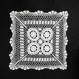 May include: White crocheted doily with a square shape and intricate floral designs.