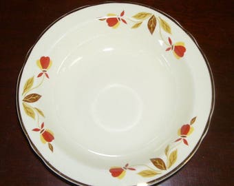 May include: A white ceramic bowl with a gold rim and a brown and yellow floral design. The bowl is decorated with a repeating pattern of leaves and flowers.