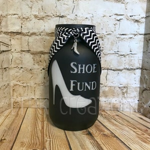 May include: Black glass jar with a white high heel shoe design and the text "Shoe Fund". The jar has a black and white chevron ribbon tied around the top with a silver shoe charm.