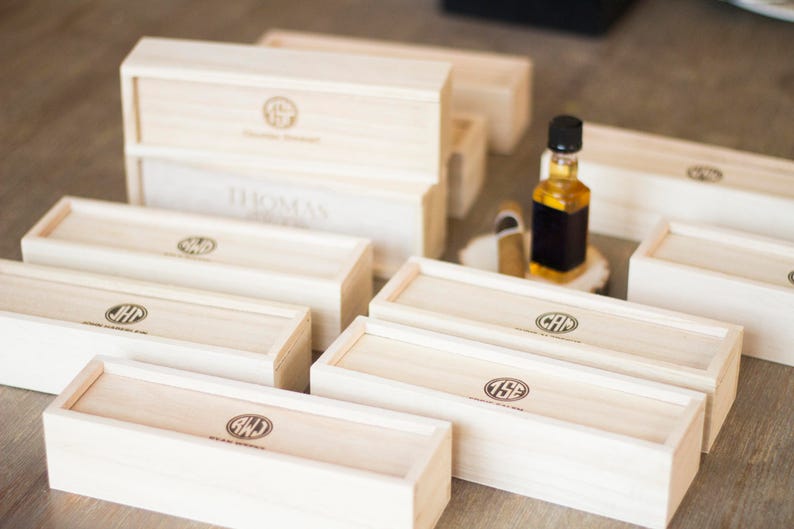 May include: A collection of wooden boxes with personalized initials and the text "Custom Engraved" on the top. The boxes are arranged in a staggered pattern on a wooden surface.