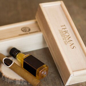 May include: Two wooden boxes with engraved text. The larger box has the text "THOMAS GROOMSMAN AUGUST 19, 2017". The smaller box has a cigar and a small bottle of liquor inside.