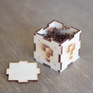 May include: A small wooden box with a question mark design on each side. The box is open and filled with brown shredded paper.