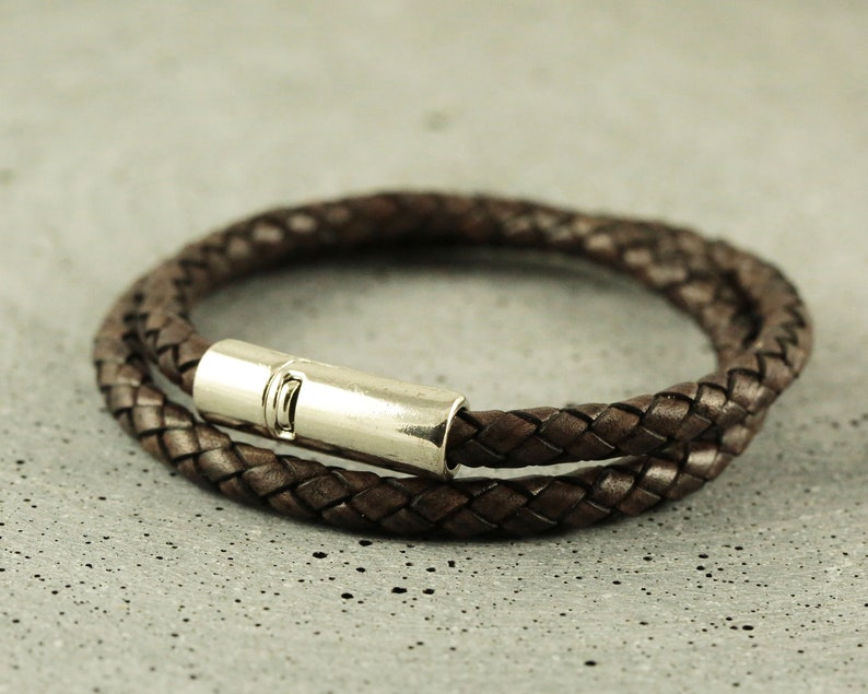 Puede incluir: Un brazalete de cuero marr&oacute;n con un cierre de plata. El brazalete est&aacute; trenzado y tiene una doble capa.