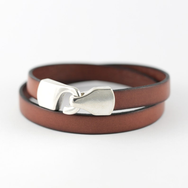 May include: A brown leather bracelet with a silver-colored clasp. The bracelet wraps around twice, showcasing the rich color of the leather. The clasp is a prominent feature, adding a touch of shine to the accessory.