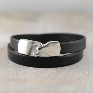 May include: A black leather bracelet with a silver clasp. The bracelet is double-layered and has a simple design.