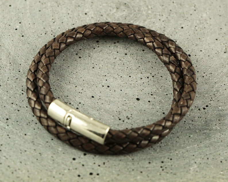 Puede incluir: Un brazalete de cuero marr&oacute;n con un dise&ntilde;o trenzado y un cierre plateado.