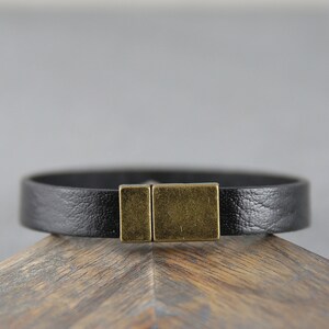 May include: A black leather bracelet with a brass clasp. The bracelet is simple and elegant.