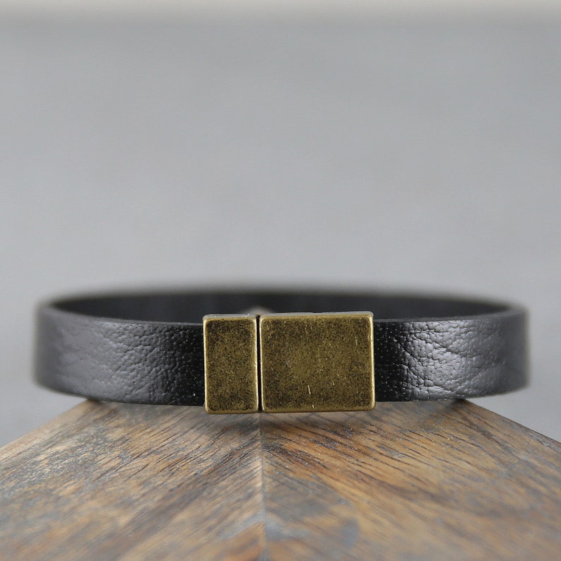 May include: A black leather bracelet with a brass clasp. The bracelet is simple and elegant.