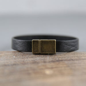 May include: A black leather bracelet with a brass clasp.