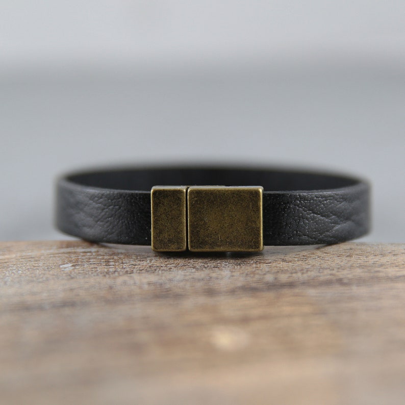 May include: A black leather bracelet with a brass clasp.