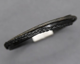 May include: A black leather bracelet with a braided design. The bracelet is made of two layers of leather, one braided and one smooth.