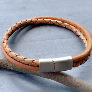 May include: A braided leather bracelet with a silver magnetic clasp. The bracelet is made of two strands of leather that are woven together.