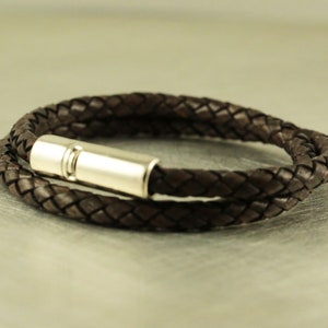 Puede incluir: Un brazalete de cuero marr&oacute;n con un cierre magn&eacute;tico plateado. El brazalete est&aacute; trenzado y tiene un dise&ntilde;o sencillo.