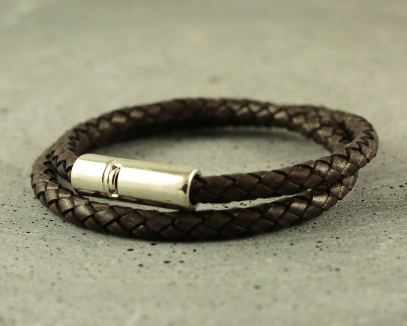 Puede incluir: Un brazalete de cuero marr&oacute;n con un cierre de plata. El brazalete est&aacute; trenzado y tiene un dise&ntilde;o sencillo.