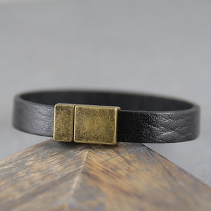 May include: A black leather bracelet with a gold-toned metal clasp.