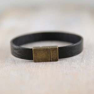 May include: A black leather bracelet with a brass magnetic clasp.
