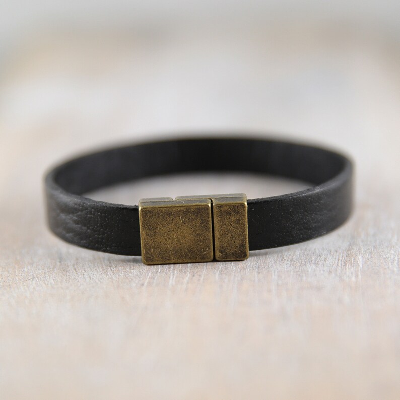 May include: A black leather bracelet with a brass magnetic clasp.