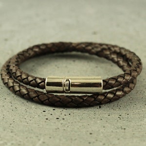 Puede incluir: Un brazalete de cuero marr&oacute;n con un cierre magn&eacute;tico plateado. El brazalete est&aacute; trenzado y tiene un dise&ntilde;o de doble vuelta.