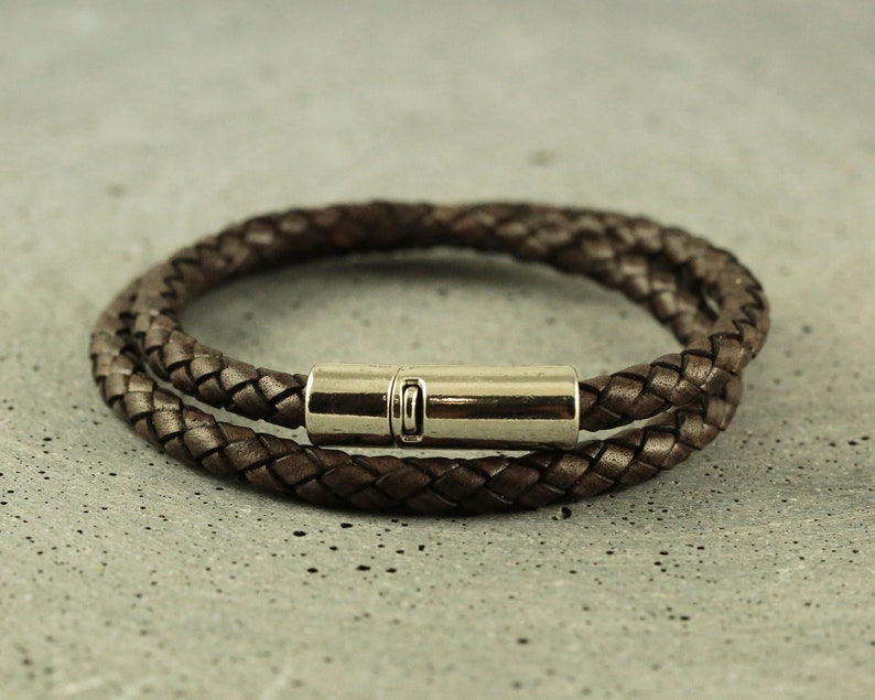 Puede incluir: Un brazalete de cuero marr&oacute;n con un cierre magn&eacute;tico plateado. El brazalete est&aacute; trenzado y tiene un dise&ntilde;o de doble vuelta.