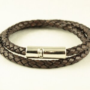 Puede incluir: Un brazalete de cuero marr&oacute;n con un dise&ntilde;o trenzado y un cierre magn&eacute;tico plateado.