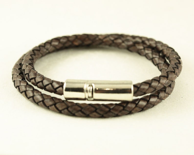 Puede incluir: Un brazalete de cuero marr&oacute;n con un dise&ntilde;o trenzado y un cierre magn&eacute;tico plateado.