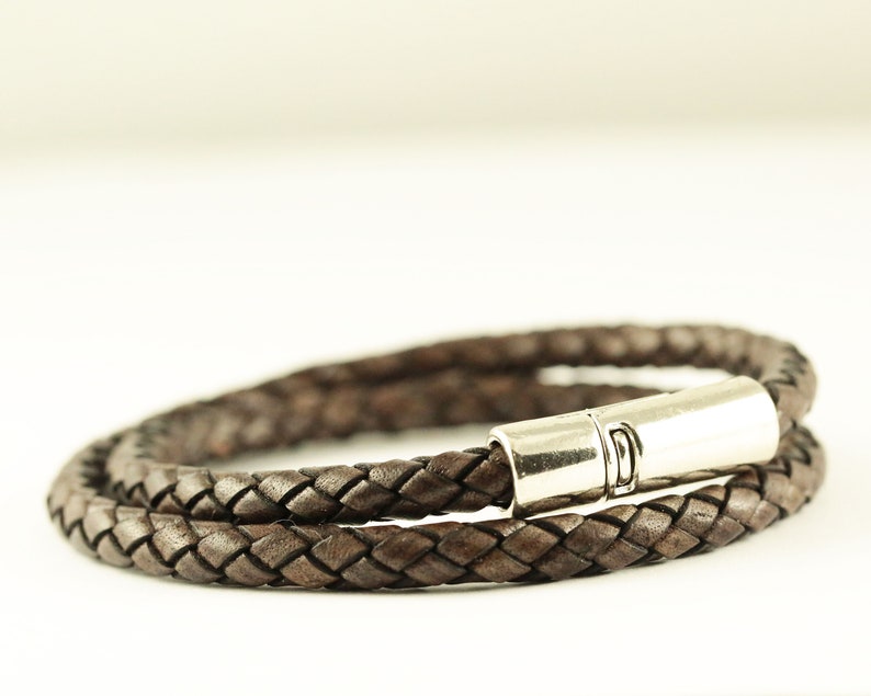 Puede incluir: Un brazalete de cuero marr&oacute;n con un cierre de plata. El brazalete est&aacute; trenzado y tiene un dise&ntilde;o sencillo.