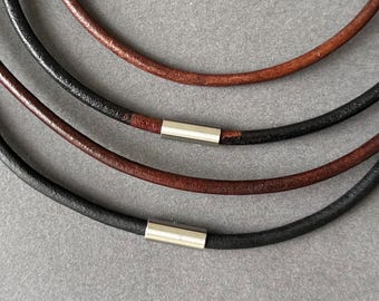 Puede incluir: Primer plano de tres collares de cuero en negro y marrón. Cada collar tiene un cierre de color plateado. Los collares están dispuestos en un estilo en capas, con los colores alternando entre negro y marrón.