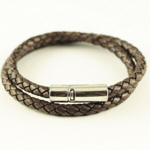 Puede incluir: Un brazalete de cuero marr&oacute;n con cierre magn&eacute;tico plateado.