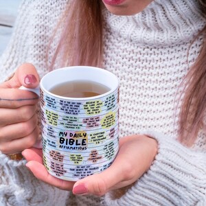 May include: White ceramic mug with a colorful design featuring the text "My Daily Bible Affirmations". The mug is filled with a light brown liquid.