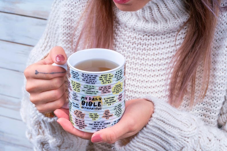 May include: White ceramic mug with a colorful design featuring the text "My Daily Bible Affirmations". The mug is filled with a light brown liquid.