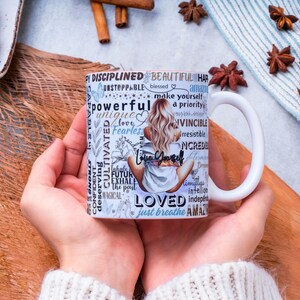Puede incluir: Taza de cer&aacute;mica blanca con un dise&ntilde;o que presenta a una mujer con cabello rubio y las palabras "Love Yourself" y otras palabras inspiradoras. La taza se sostiene con dos manos, con un fondo de palitos de canela, an&iacute;s estrellado y un cruas&aacute;n.