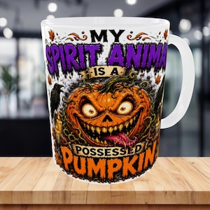 May include: A white ceramic mug featuring a graphic of a sinister orange pumpkin with a wide, toothy grin and a purple tongue. The text reads MY SPIRIT ANIMAL IS A POSSESSED PUMPKIN, accompanied by illustrations of black ravens and autumn leaves.