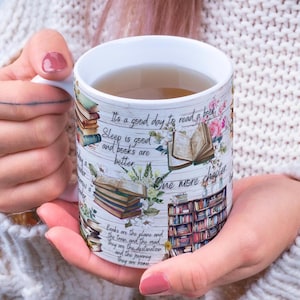 Op de afbeelding: Witte keramische mok met een boekenthema. De mok heeft stapels boeken, open boeken en een boekenplankillustratie, samen met de tekst "It's a good day to read a book." en "One more chapter."