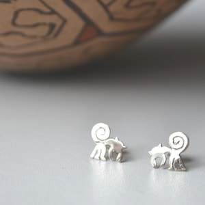 Puede incluir: Un par de pendientes de plata con un diseño de animal estilizado. Los pendientes son pequeños y delicados, con una cola rizada y un cuerpo detallado.