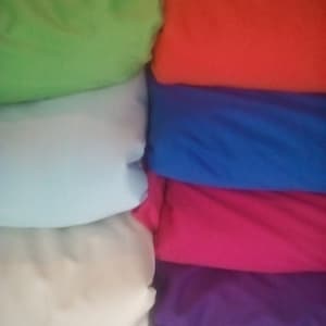 May include: Stack of six fabric swatches in different colors: green, light blue, white, pink, purple, and red.