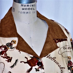 May include: A cream-colored jacket with a brown suede collar. The jacket features a western-themed print with cowboys riding horses and the words "Texas", "Nebraska", and "Nevada".