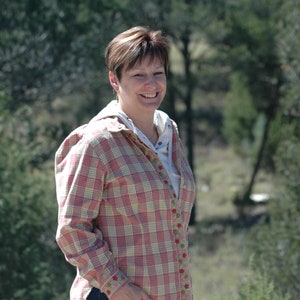 May include: A woman wearing a pink and white plaid shirt with floral embroidery. She is smiling and looking at the camera.