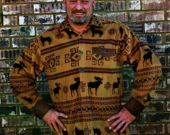 May include: A button-down shirt with a tan and brown pattern featuring moose silhouettes and geometric designs. The shirt has a brown pocket and cuffs, and is worn with blue jeans. The shirt is made of a soft, comfortable material.