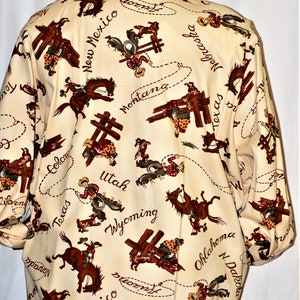 May include: A cream-colored jacket with a brown suede collar features a repeating pattern of cowboys riding horses and lassoing steers. The pattern includes the names of various states, including Texas, Montana, Wyoming, and New Mexico.
