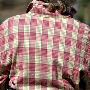 May include: A person wearing a red and white plaid shirt with a silver belt featuring turquoise and red stones.